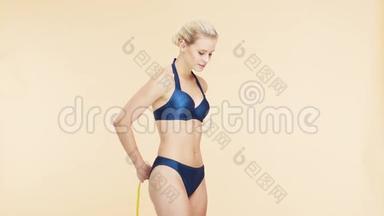 年轻、美丽、健康、自然的金发碧眼的女人，穿着蓝色泳衣，测量着她完美的身材。运动、健身、护肤